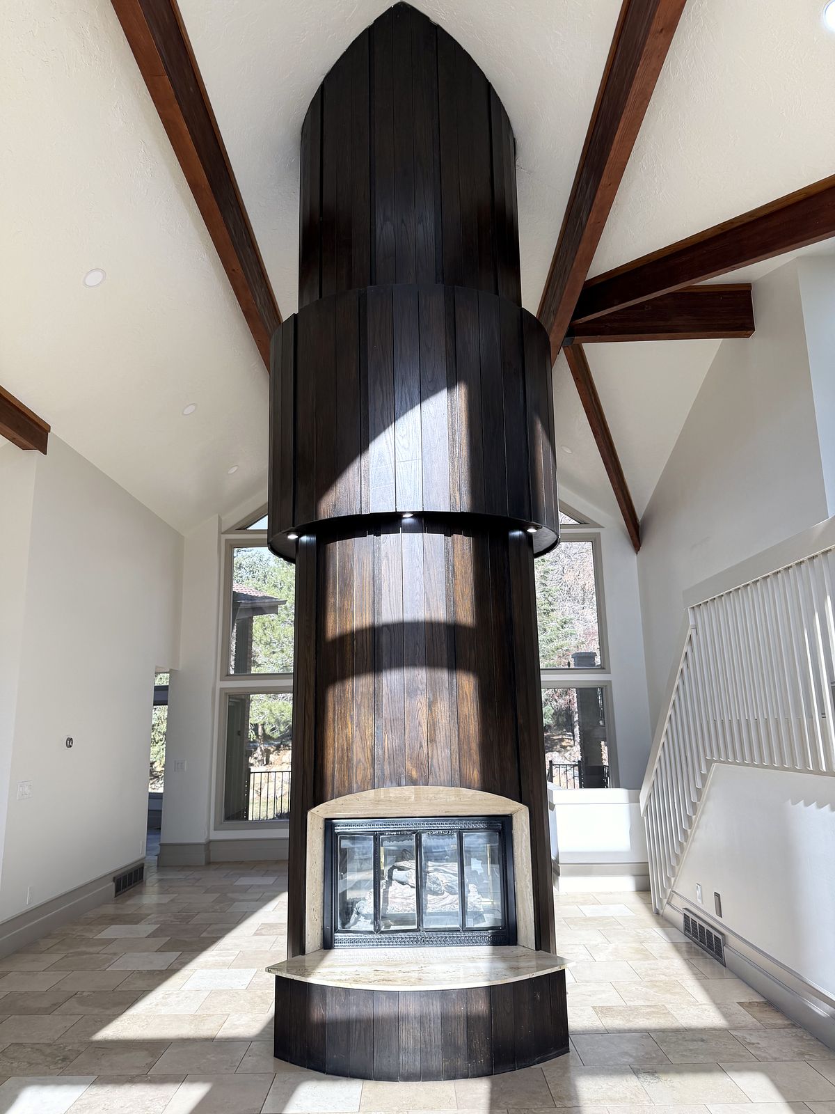 Sculptural wood-clad fireplace column rising to a vaulted ceiling with exposed beams and angled windows